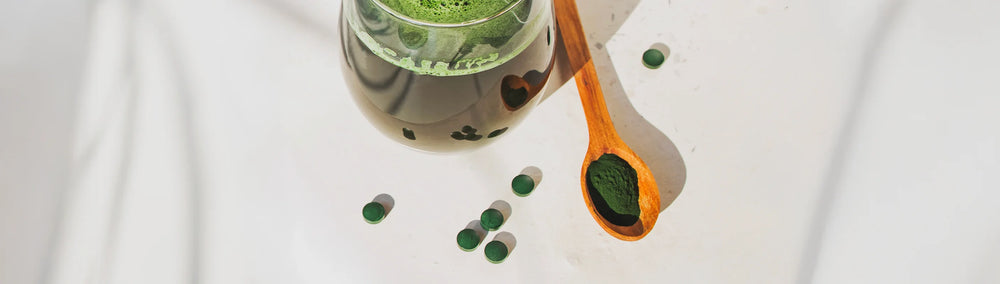 Verre avec poudre de spiruline dans une cuillère et quelques comprimés